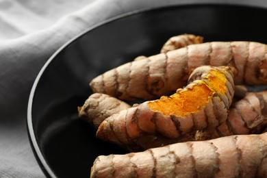 Photo of Many raw turmeric roots in black bowl, closeup