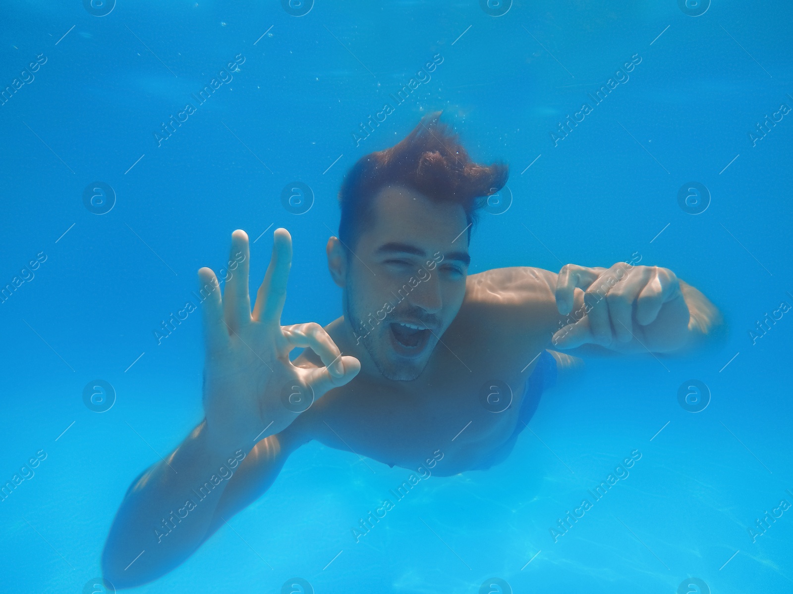 Photo of Handsome young man swimming in pool, underwater view