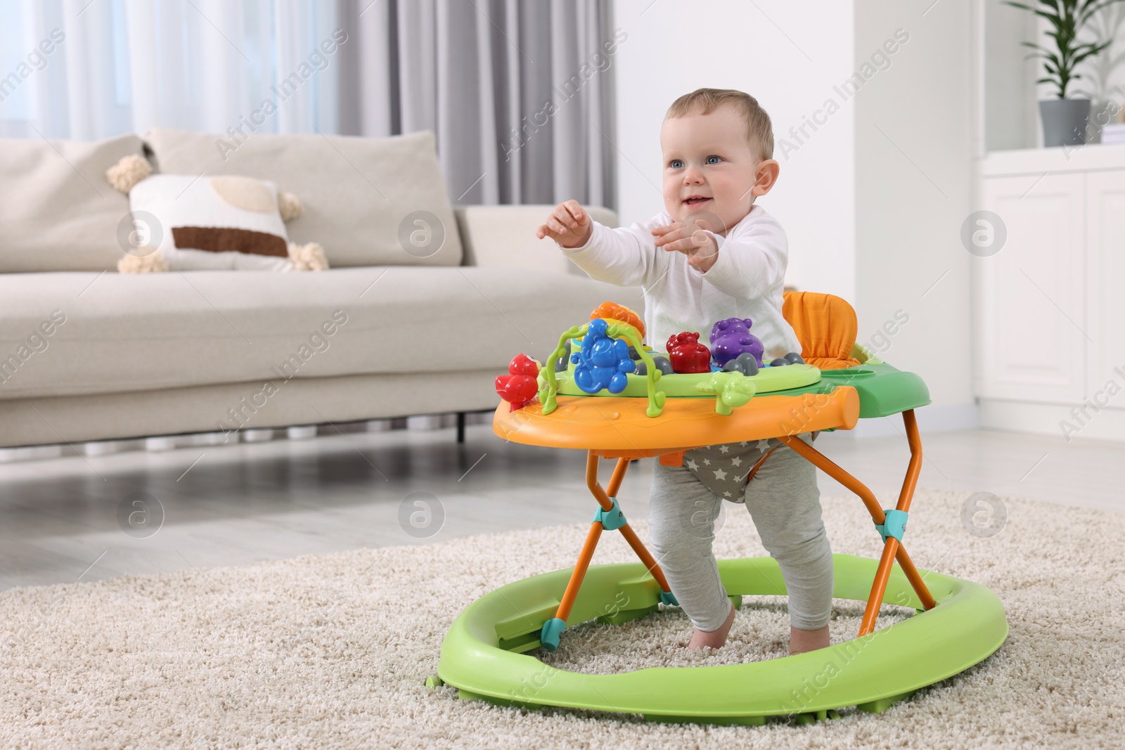 Photo of Cute baby making first steps with toy walker at home, space for text