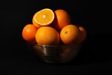 Photo of Bowl with ripe juicy oranges on black background