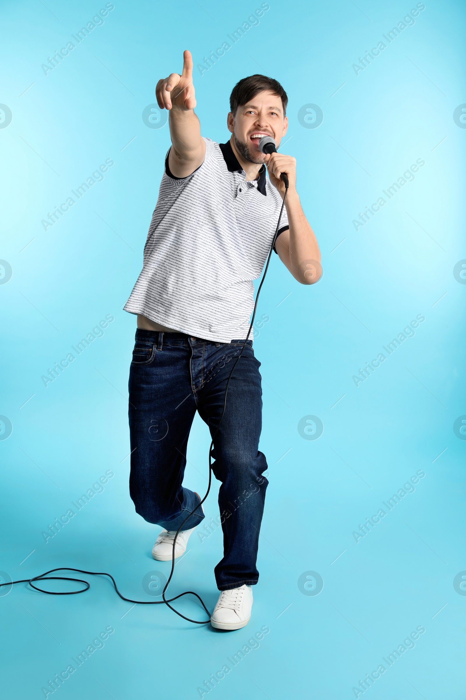 Photo of Handsome man in casual clothes singing with microphone on color background