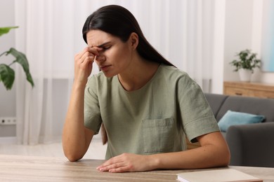 Photo of Sad woman suffering from headache at wooden table indoors