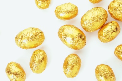 Photo of Many chocolate eggs wrapped in bright golden foil on white background, top view