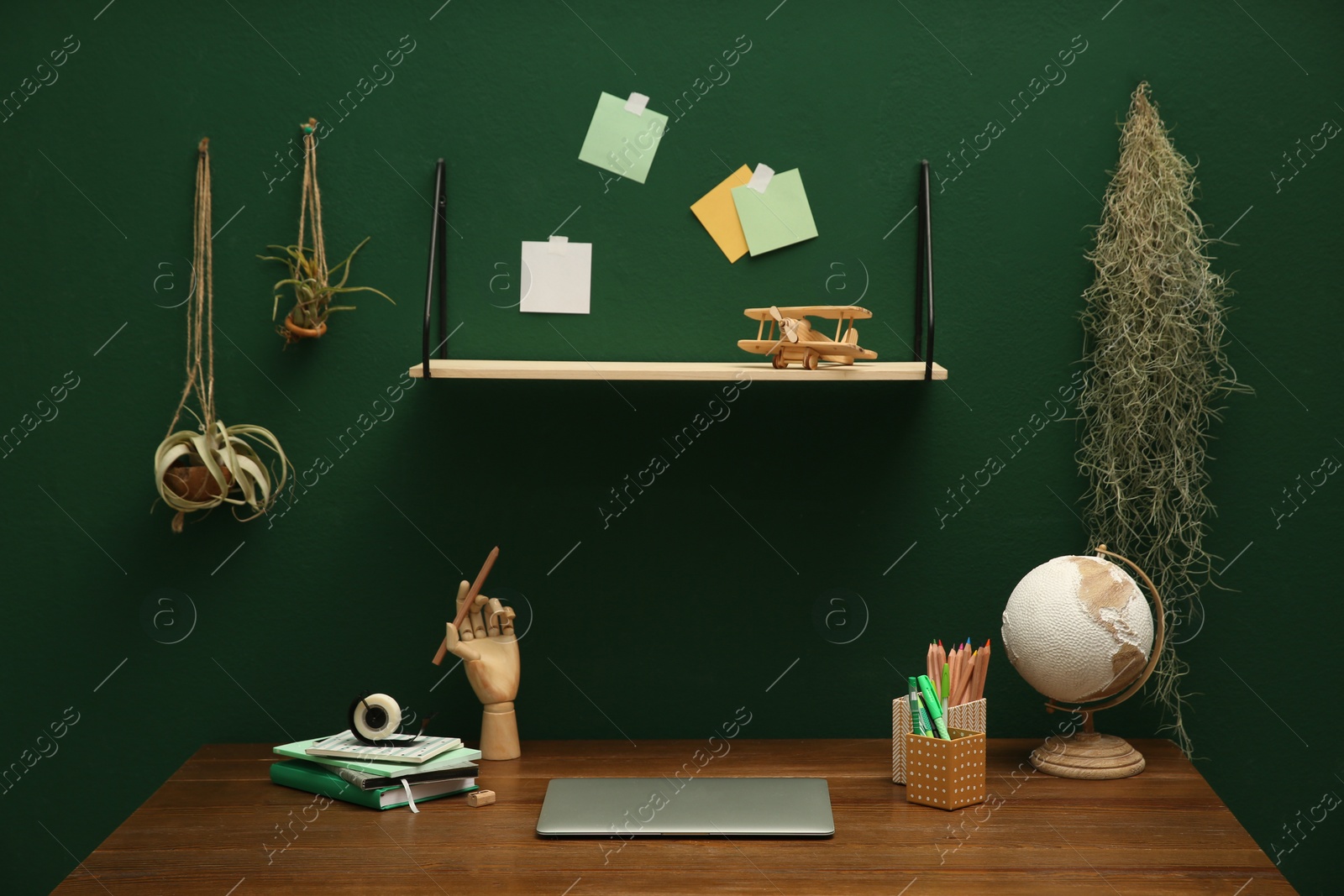 Photo of Stylish workplace with laptop on wooden desk and different decor near green wall. Interior design