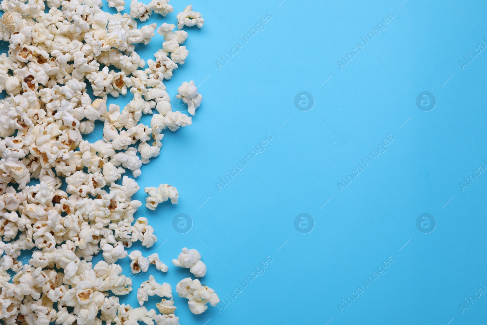Photo of Tasty popcorn on light blue background, flat lay. Space for text