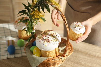 Woman putting traditional Easter cake in basket at table, closeup