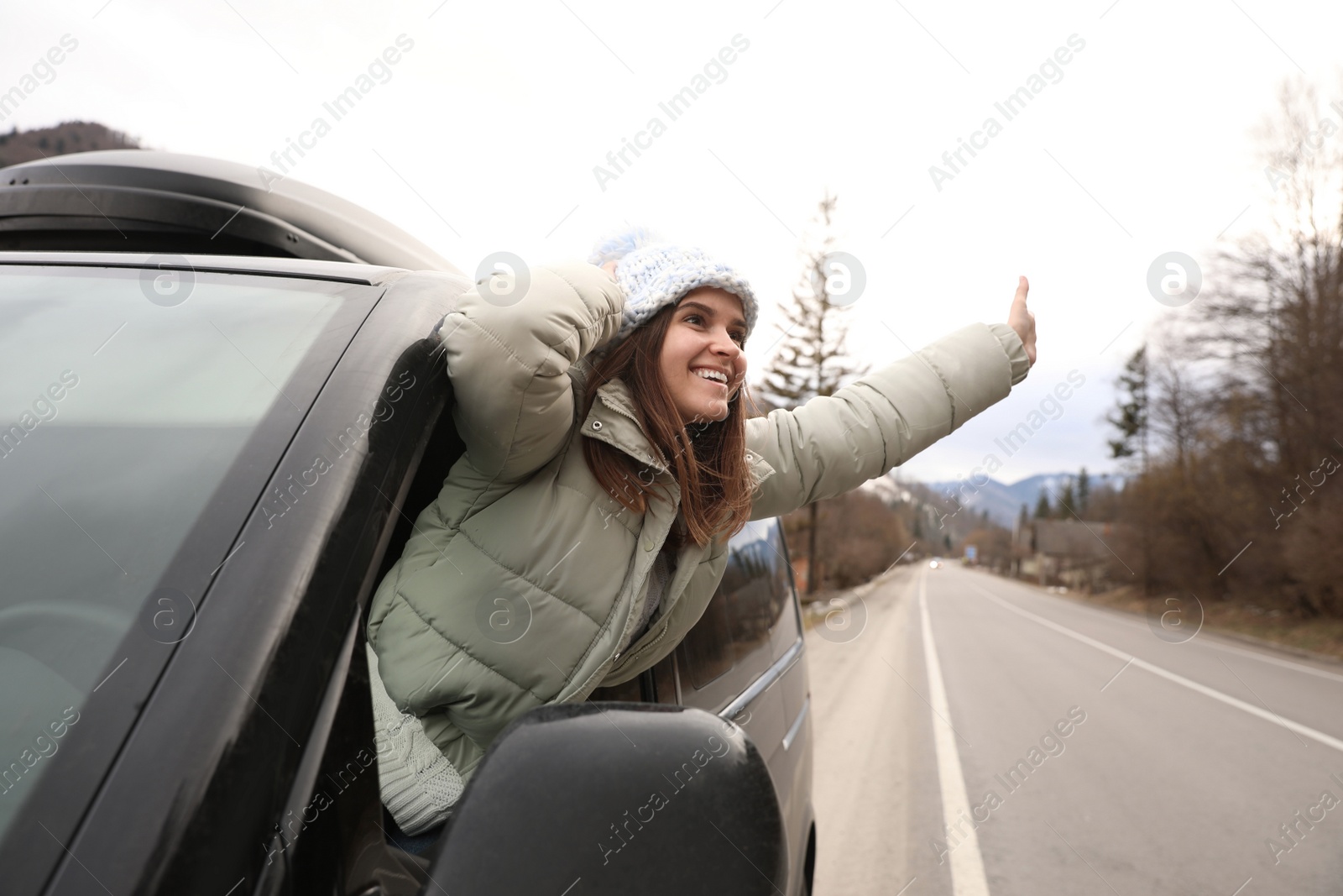 Photo of Happy woman leaning out of car window on road. Winter vacation