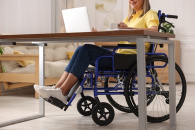 Photo of Woman in wheelchair with cup of drink using laptop at home, closeup
