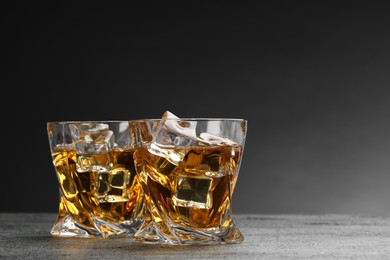 Photo of Whiskey and ice cubes in glasses on grey textured table, closeup. Space for text