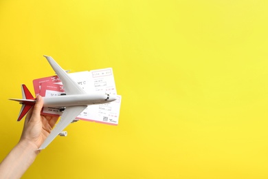 Woman holding toy airplane and tickets on yellow background, closeup. Space for text