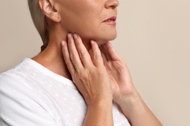 Photo of Mature woman doing thyroid self examination on beige background closeup