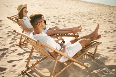 Photo of Young couple relaxing in deck chairs on sandy beach