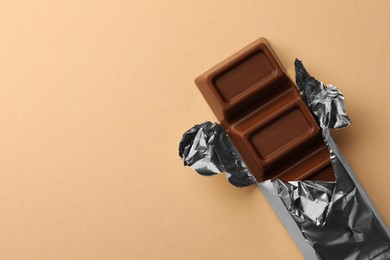 Delicious chocolate bar wrapped in foil on beige background, top view. Space for text