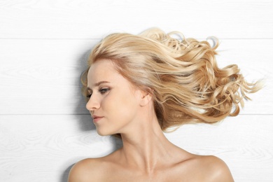 Photo of Beautiful woman with healthy long blonde hair on light wooden background, top view