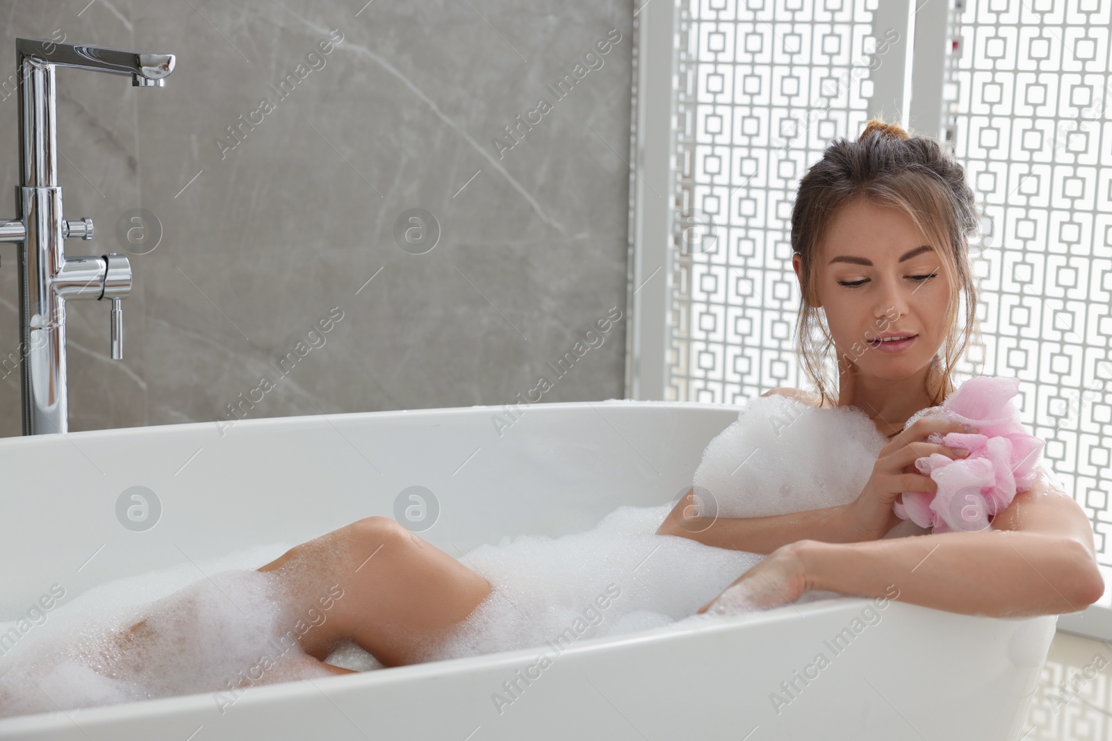 Photo of Beautiful woman with mesh pouf taking bath indoors, space for text