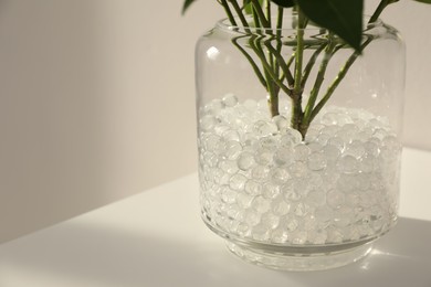 White filler with green branches in glass vase on table, space for text. Water beads