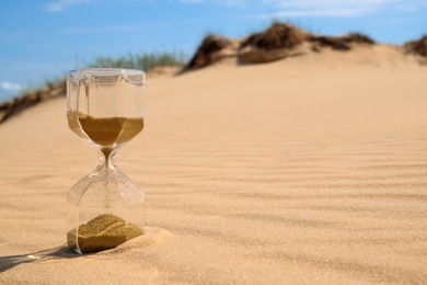 Photo of Hourglass with flowing sand in desert on sunny day. Space for text