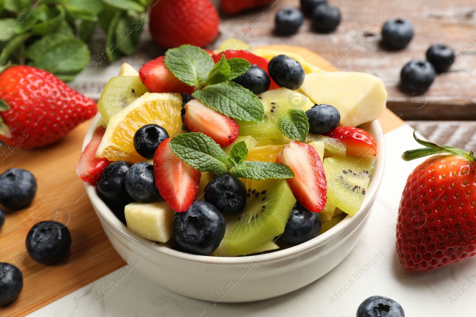 Photo of Tasty fruit salad in bowl and ingredients on wooden table, closeup