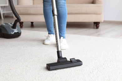 Photo of Woman cleaning carpet with vacuum in living room