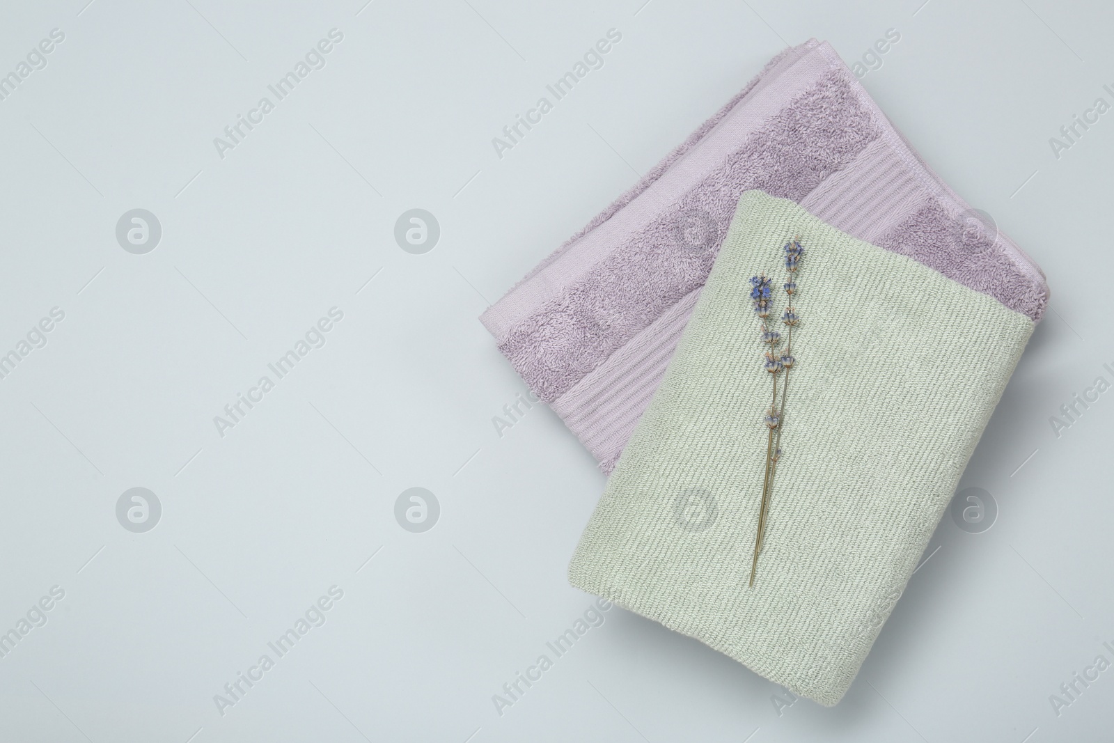 Photo of Different soft towels and lavender flowers on light grey background, top view. Space for text