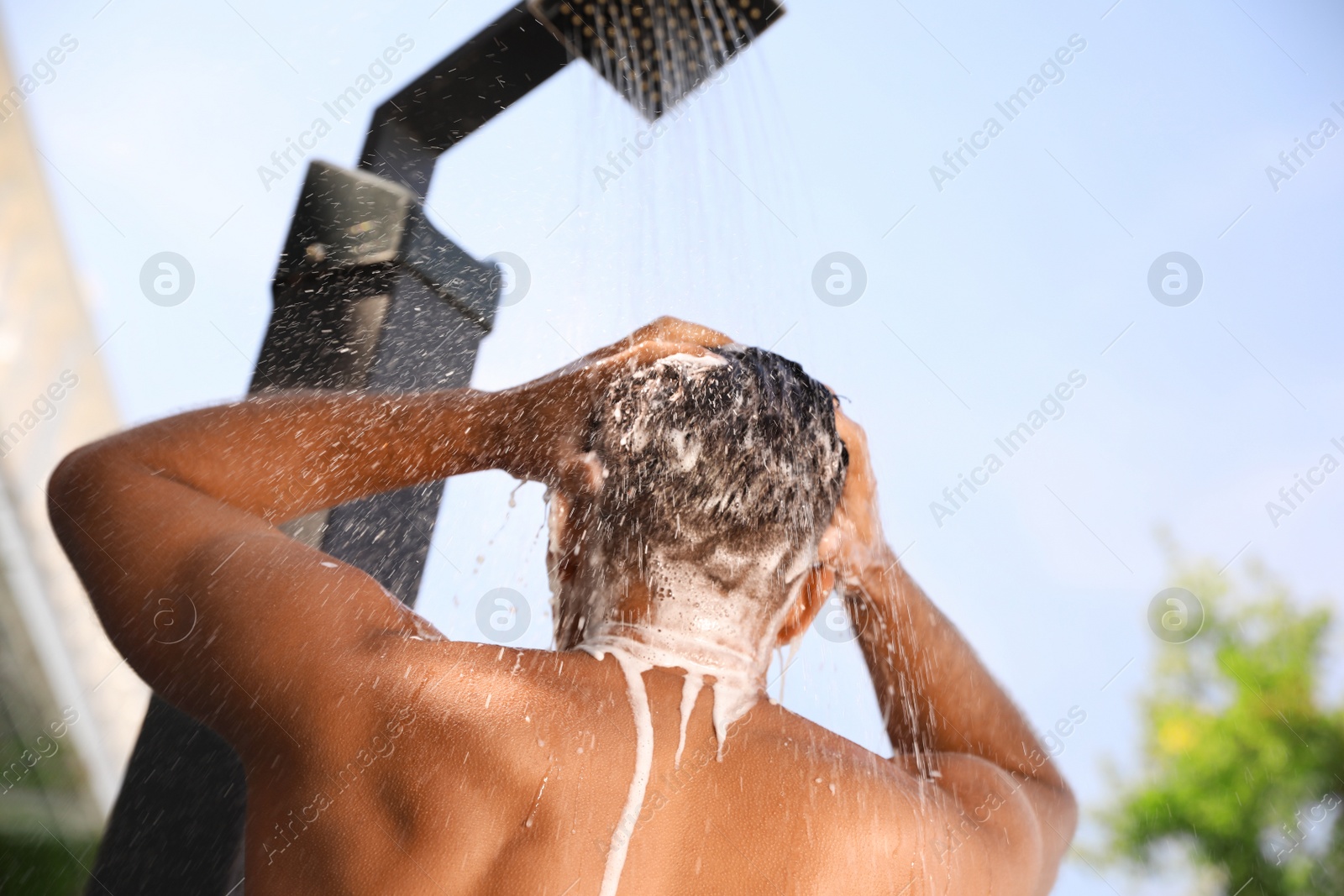 Photo of Man washing hair in outdoor shower on summer day