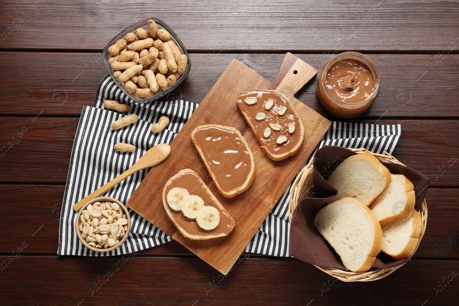 Photo of Toasts with tasty nut butter, banana slices and peanuts on wooden table, flat lay