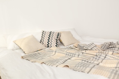 Photo of Bed with pillows and plaid near light wall. Cozy interior design