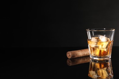 Photo of Glass of whiskey with ice cubes and cigar on black mirror surface. Space for text
