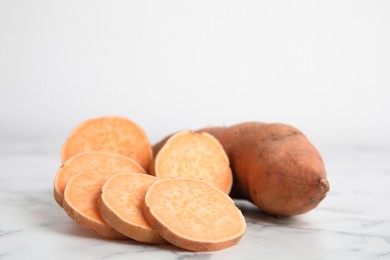Photo of Whole and cut ripe sweet potatoes on white marble table