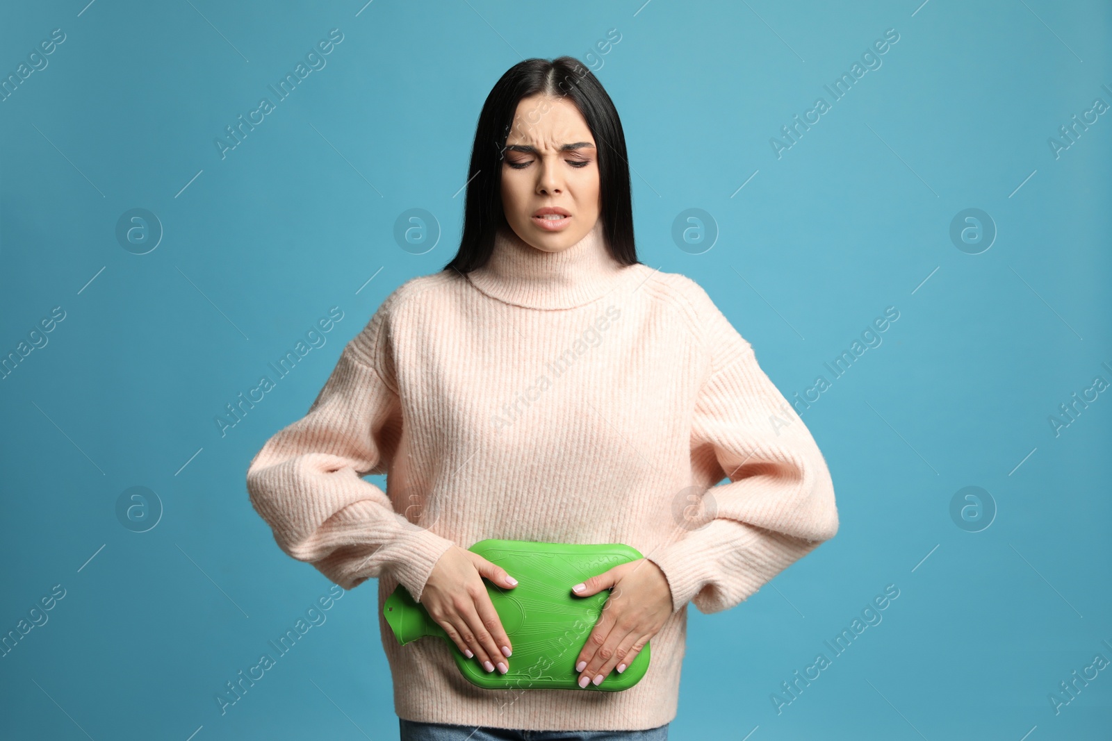 Photo of Woman using hot water bottle to relieve menstrual pain on light blue background