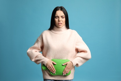 Woman using hot water bottle to relieve menstrual pain on light blue background