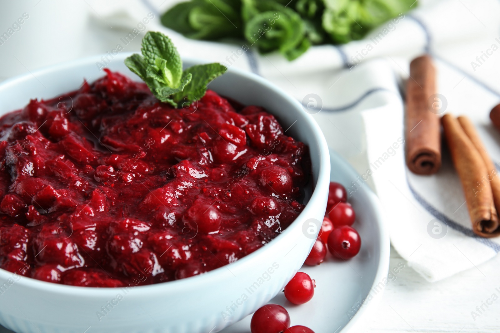 Photo of Bowl of tasty cranberry sauce with mint on table, closeup