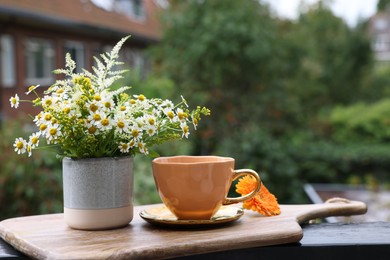 Photo of Cup of delicious chamomile tea and fresh flowers outdoors. Space for text