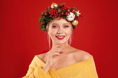 Beautiful young woman wearing Christmas wreath on red background