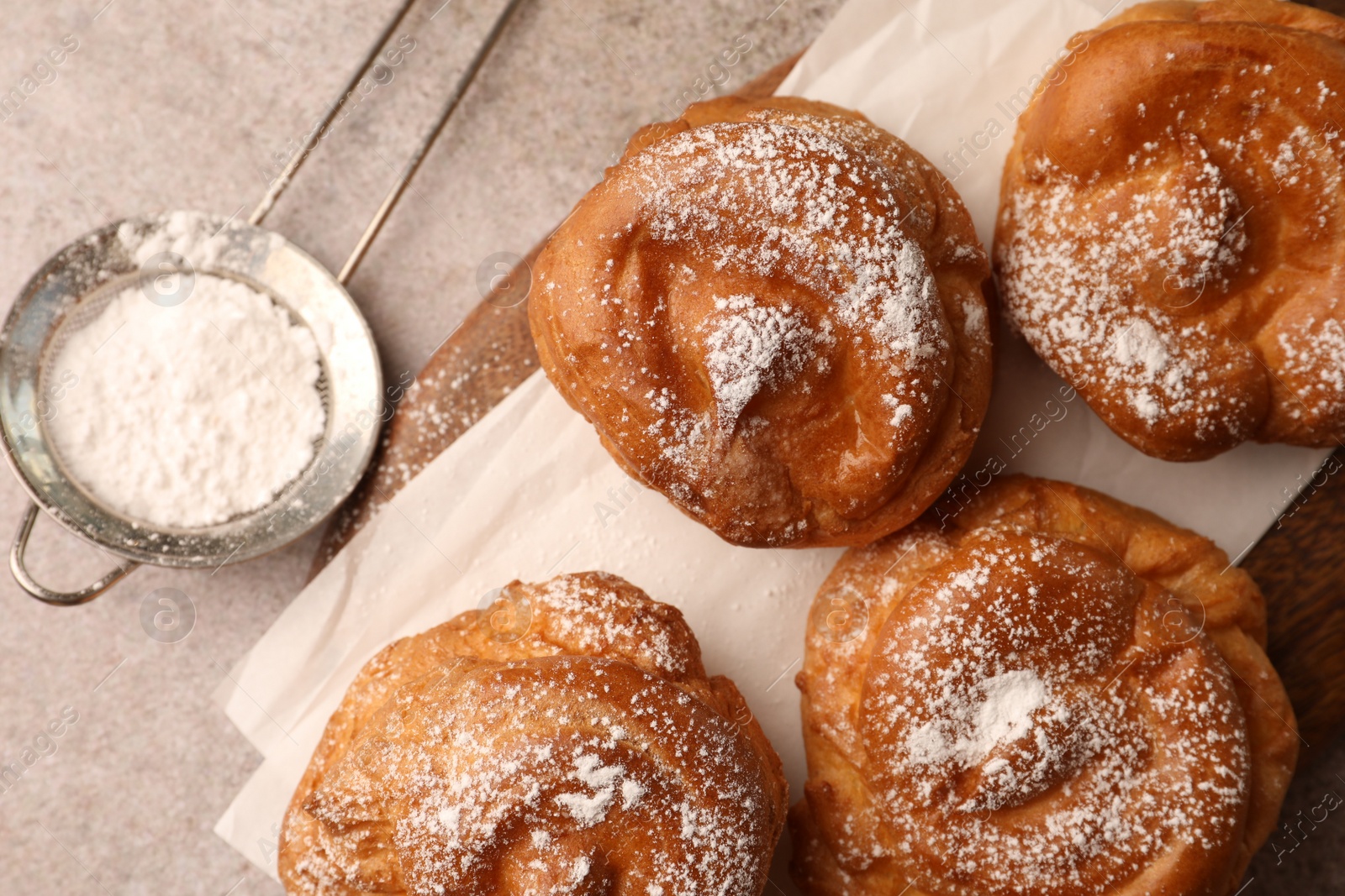 Photo of Delicious profiteroles with powdered sugar on grey table, flat lay