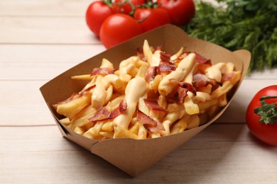 Photo of Tasty potato fries, cheese sauce, bacon and products in paper container on light wooden table, closeup