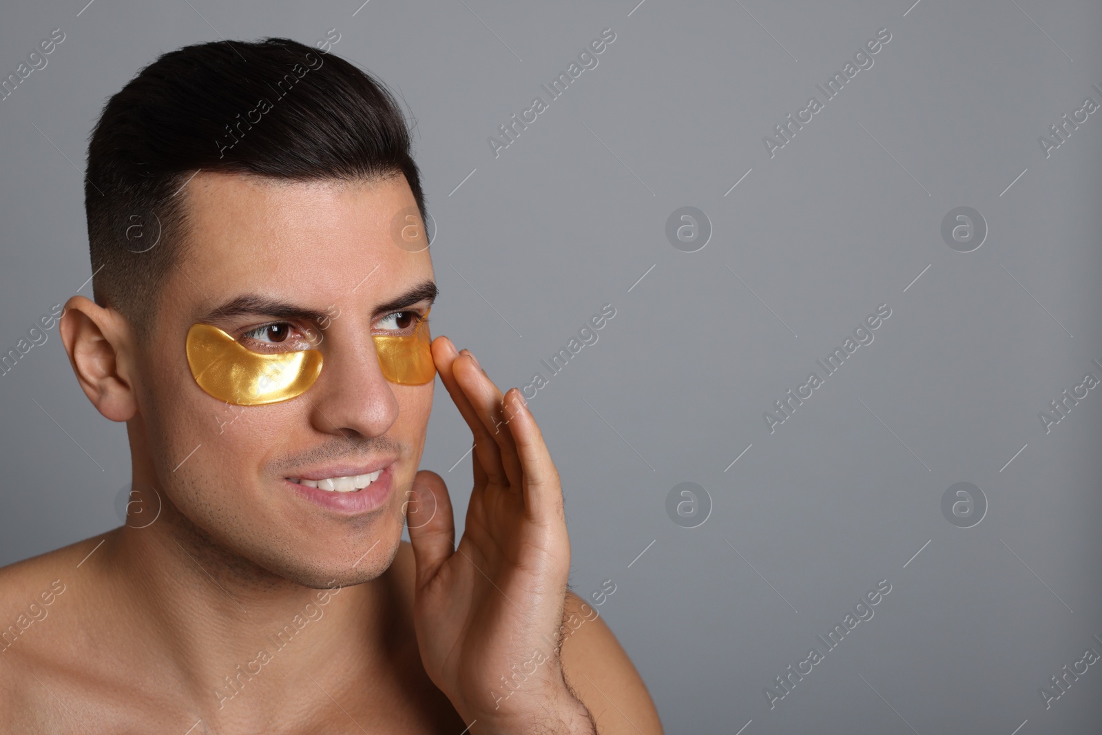 Photo of Man applying golden under eye patch on grey background. Space for text