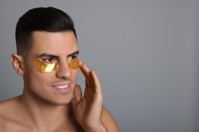 Man applying golden under eye patch on grey background. Space for text