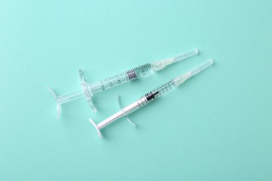 Photo of Injection cosmetology. Two medical syringes on turquoise background, top view