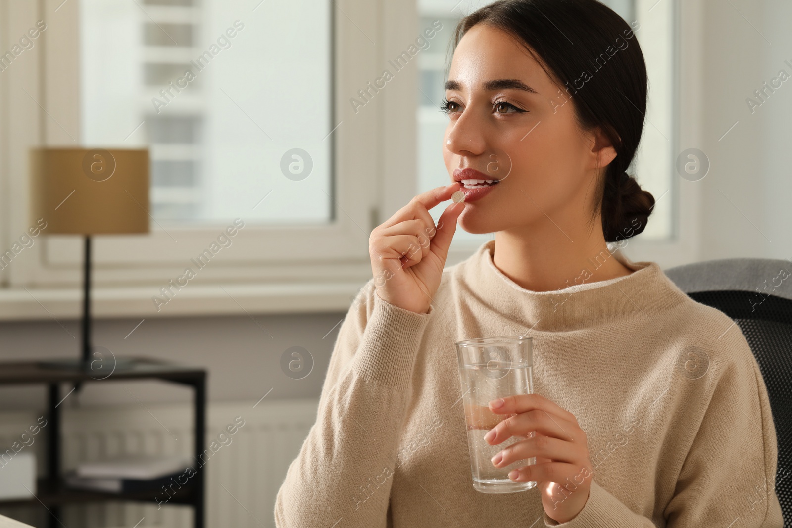 Photo of Young woman with glass of water taking dietary supplement pill indoors, space for text