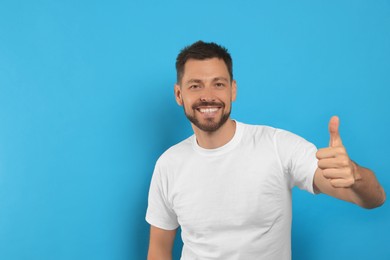 Photo of Man showing thumb up on light blue background, space for text
