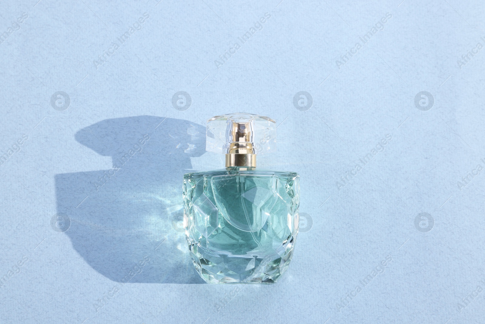 Photo of Luxury women's perfume. Sunlit glass bottle on grey background, top view