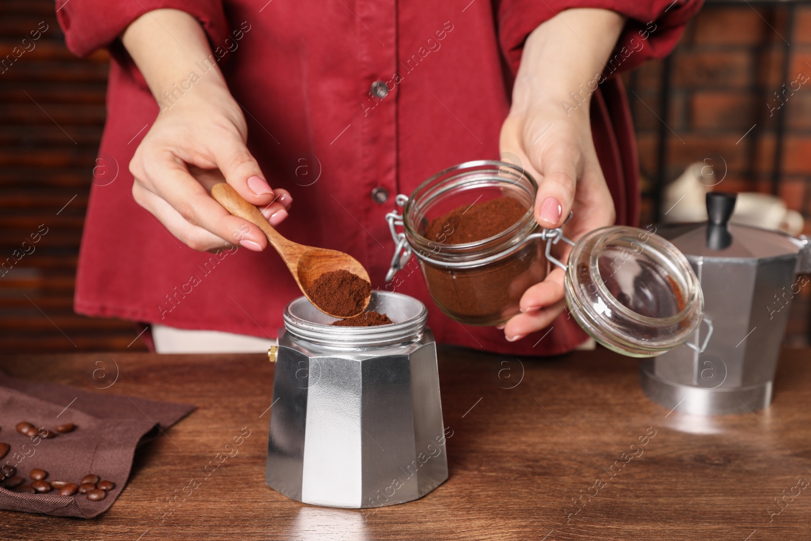 Photo of Woman putting ground coffee into moka pot at wooden table, closeup