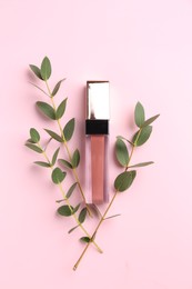 Photo of Bright lip gloss and green twigs on pink background, top view