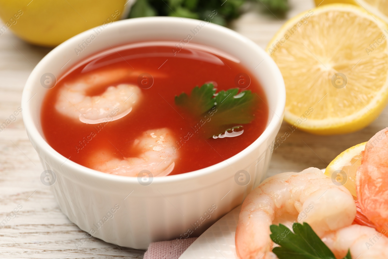 Photo of Tasty boiled shrimps with cocktail sauce, chili and parsley on light wooden table, closeup