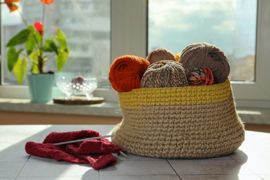 Photo of Soft woolen yarns, knitting and needles on white tiled table near window indoors