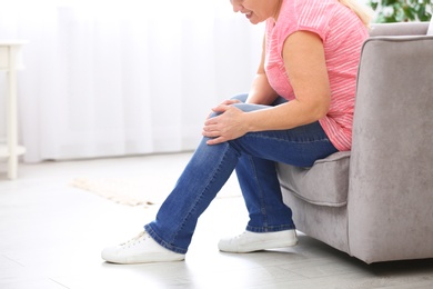 Photo of Senior woman suffering from knee pain at home, closeup. Space for text