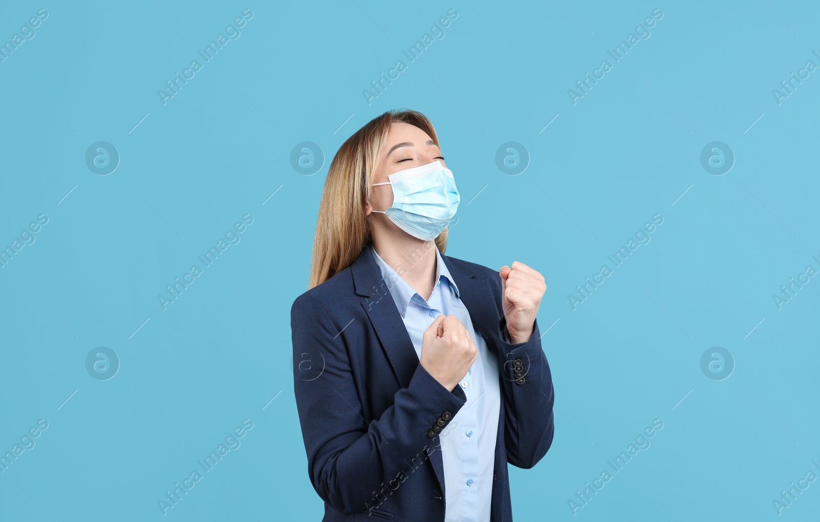 Photo of Emotional businesswoman with protective mask on light blue background. Strong immunity concept
