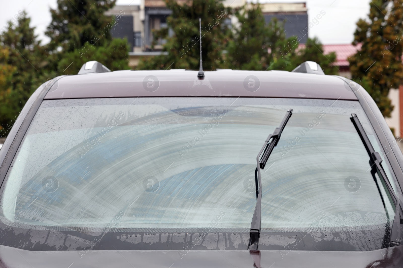 Photo of Car wipers cleaning water drops from windshield glass outdoors, closeup