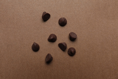 Delicious chocolate chips on brown background, top view